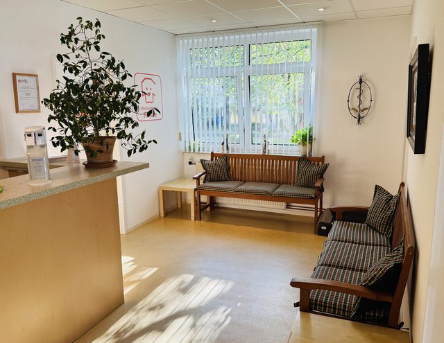 Wartebereich mit Empfangstresen, Sitzbänken und großer Fensterfront